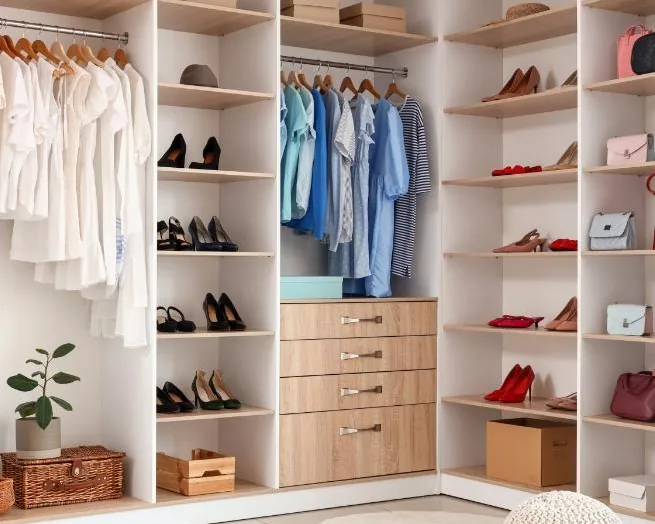 Un dressing organisé : chemises claires suspendues, chaussures alignées sur des étagères en bois clair, paniers et boîtes rangés